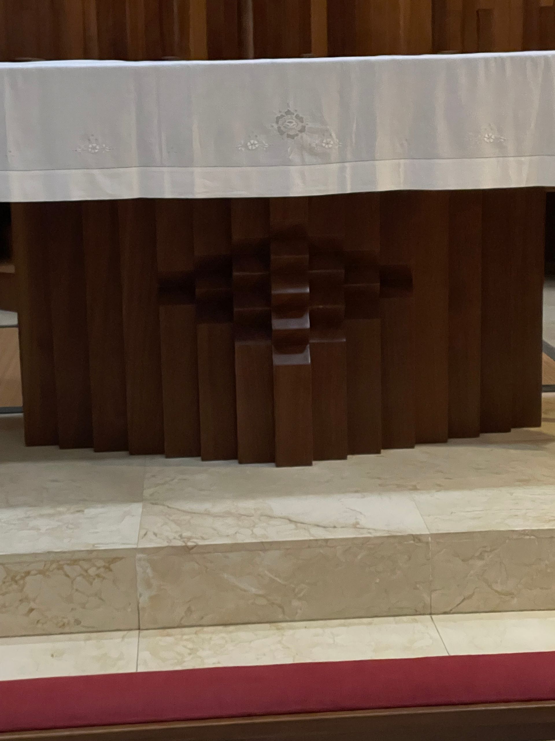 Altar de madera con mantel blanco sobre plataforma de azulejos, en una iglesia.