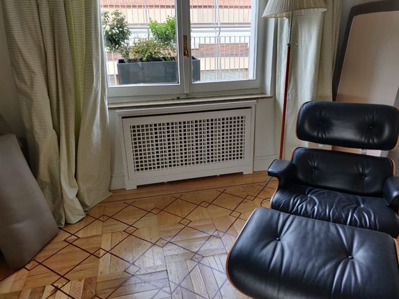 Sillón y otomana de cuero negro junto a una ventana con cortinas y una cubierta decorativa para radiador.