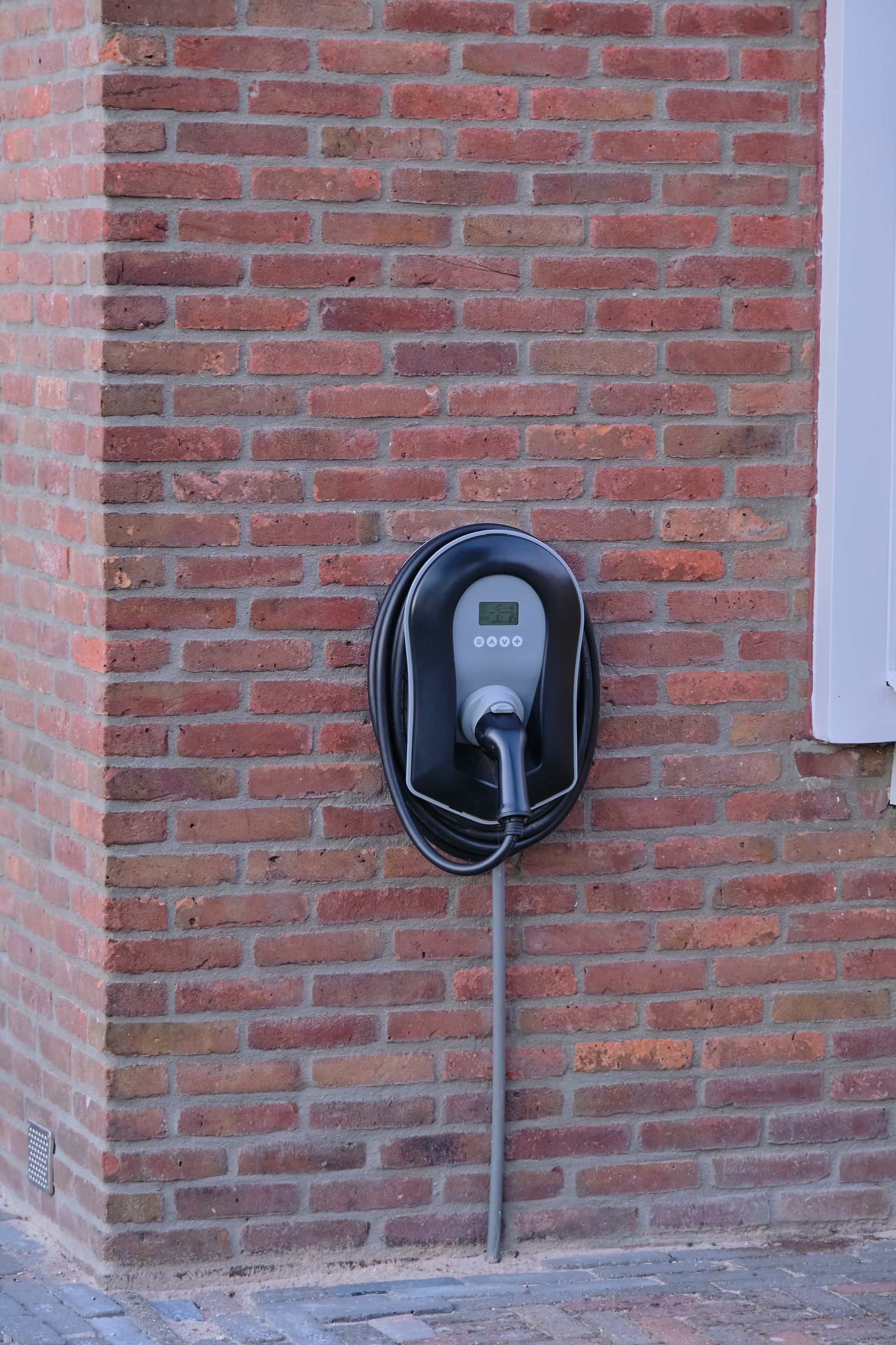 Borne de recharge murale pour véhicule électrique sur le mur de brique rouge d'une maison individuelle