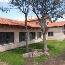 Una casa grande con techo de tejas rojas y árboles delante de ella.