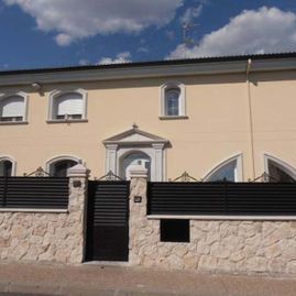 Una casa con un muro de piedra y una valla negra alrededor