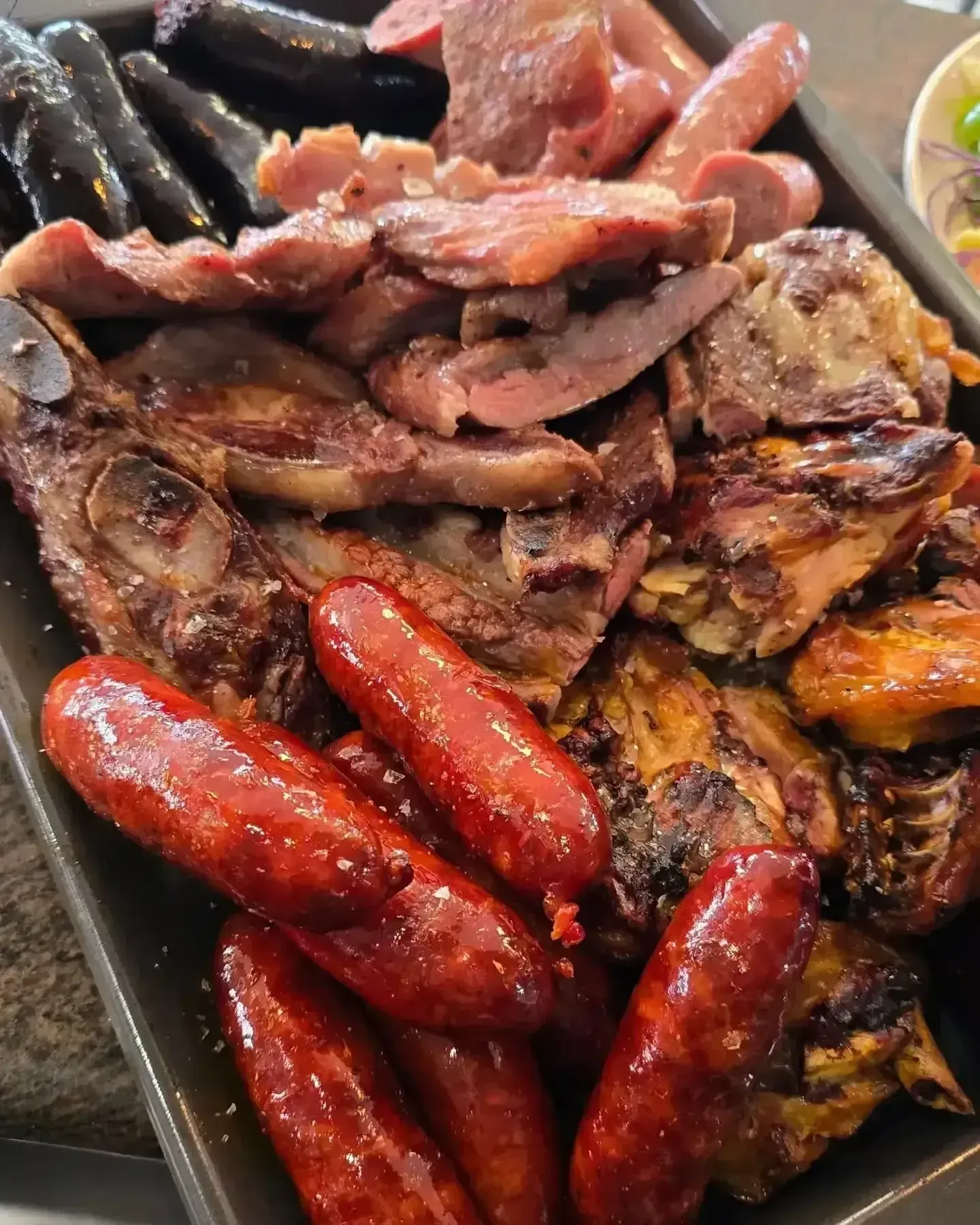 Una bandeja de carnes a la parrilla, que incluye salchichas, cerdo y pollo