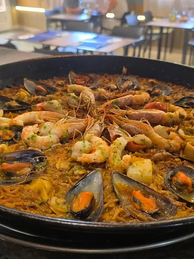 Paella de mariscos en una sartén grande de color negro; camarones, mejillones y otros mariscos encima.