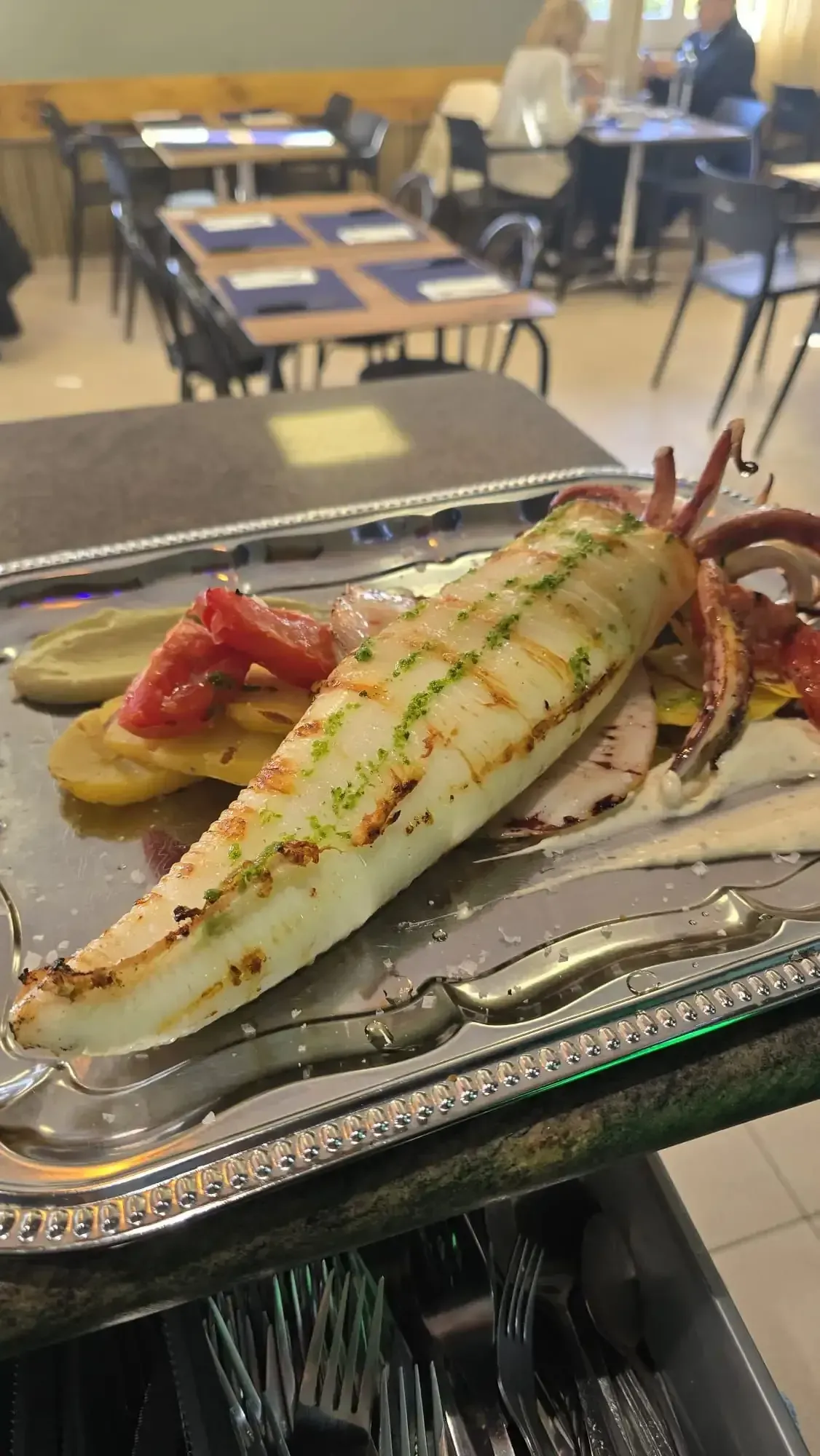 Calamares a la plancha con tomate y patatas en bandeja de plata en un restaurante.