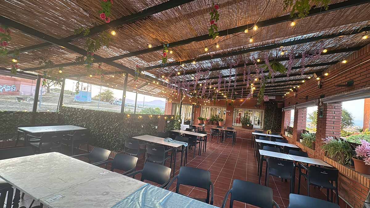 Zona de comedor exterior cubierta, con guirnaldas de luces, mesas y sillas bajo un techo de madera