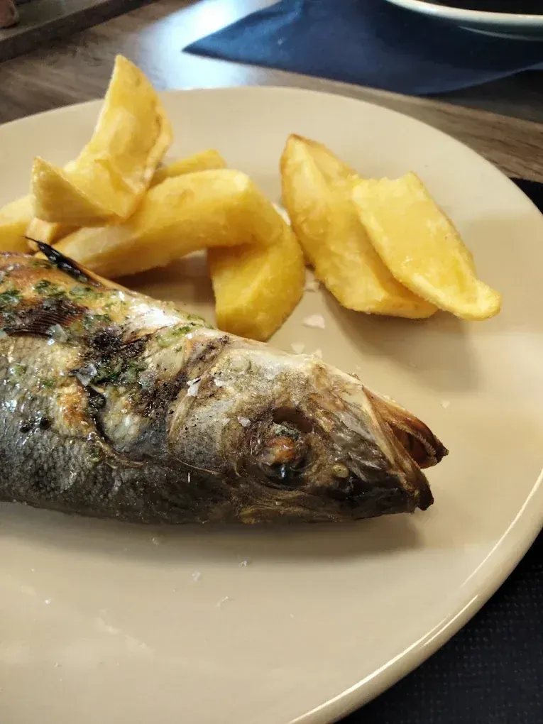 Pescado a la parrilla con gajos de patatas en un plato beige.