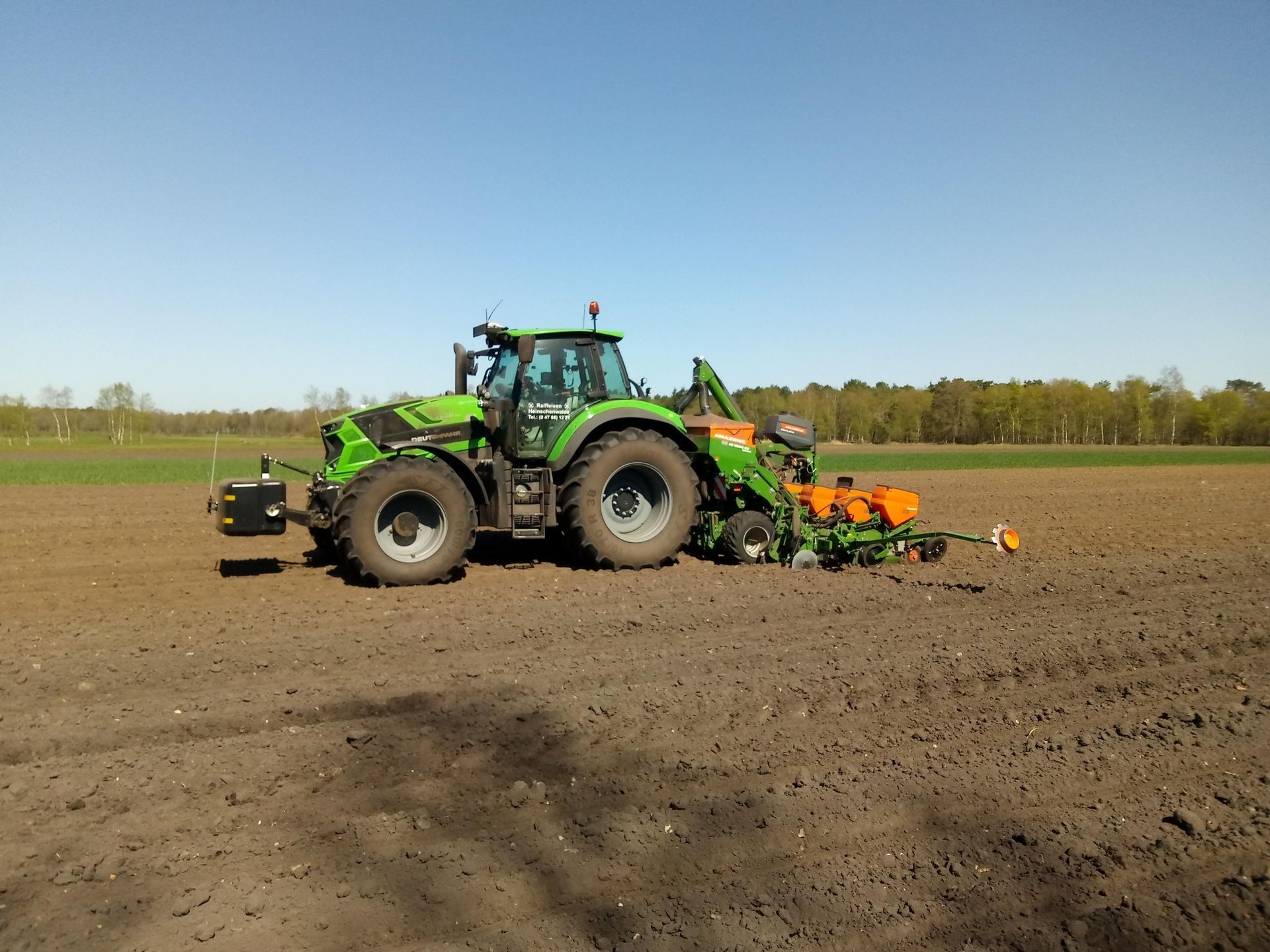 Ein grüner Traktor pflügt ein Feld, an dem eine Pflanzmaschine befestigt ist