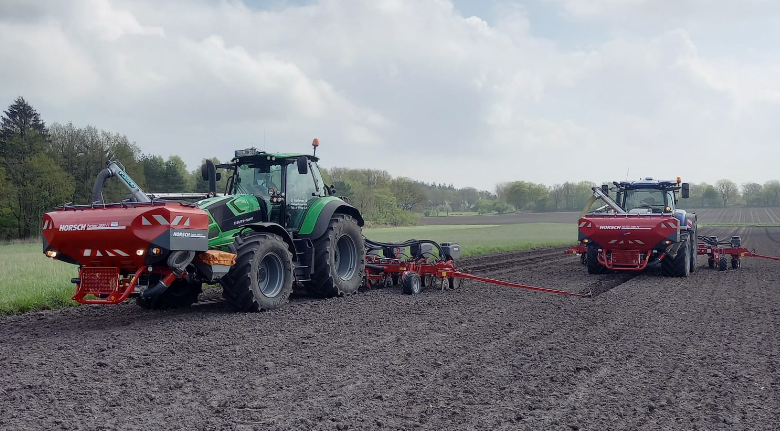 Ein grüner Traktor pflügt ein Feld, an dem eine Pflanzmaschine befestigt ist