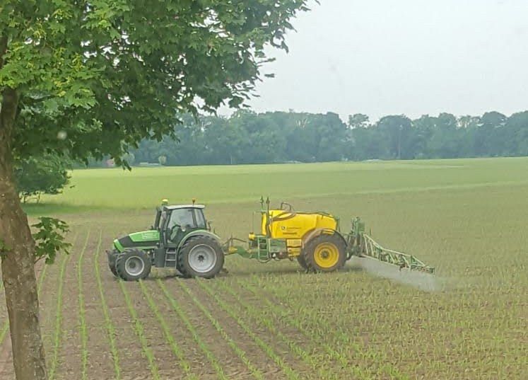 Ein Traktor besprüht ein Feld mit einem gelben Tank.
