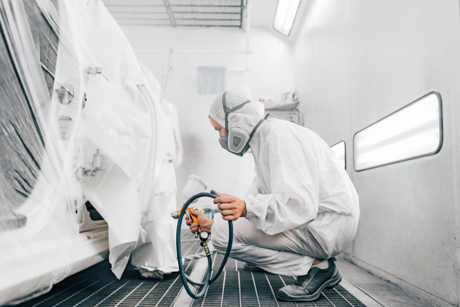 Une personne en combinaison en train de peindre une pièce de la carrosserie d'un véhicule