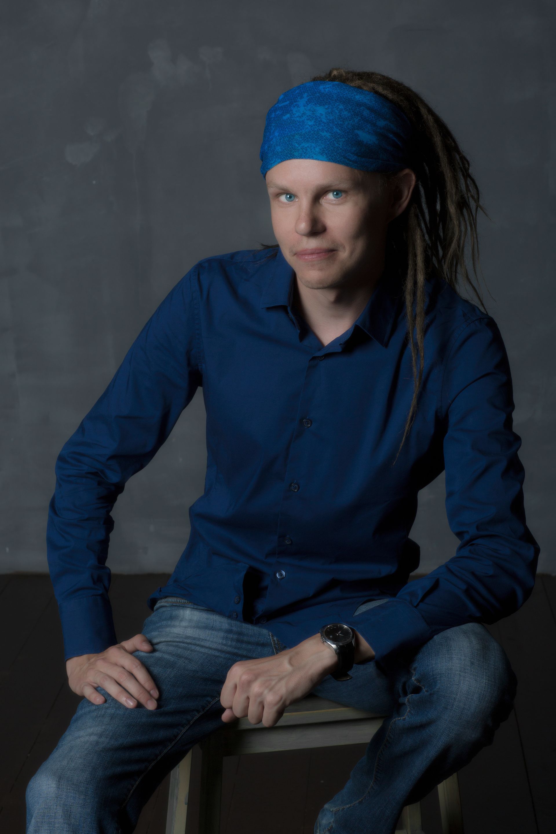 Portrait d'un jeune adulte en jean et chemise coiffé de dreadlocks et bandana bleu.