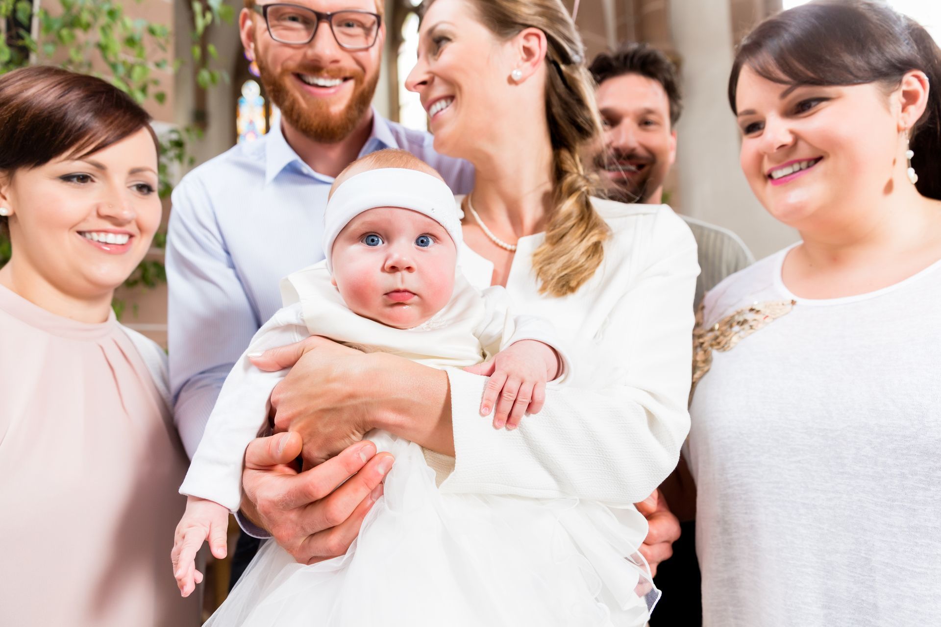 Un bébé habillé de blanc et entouré par sa famille lors d'un baptême.