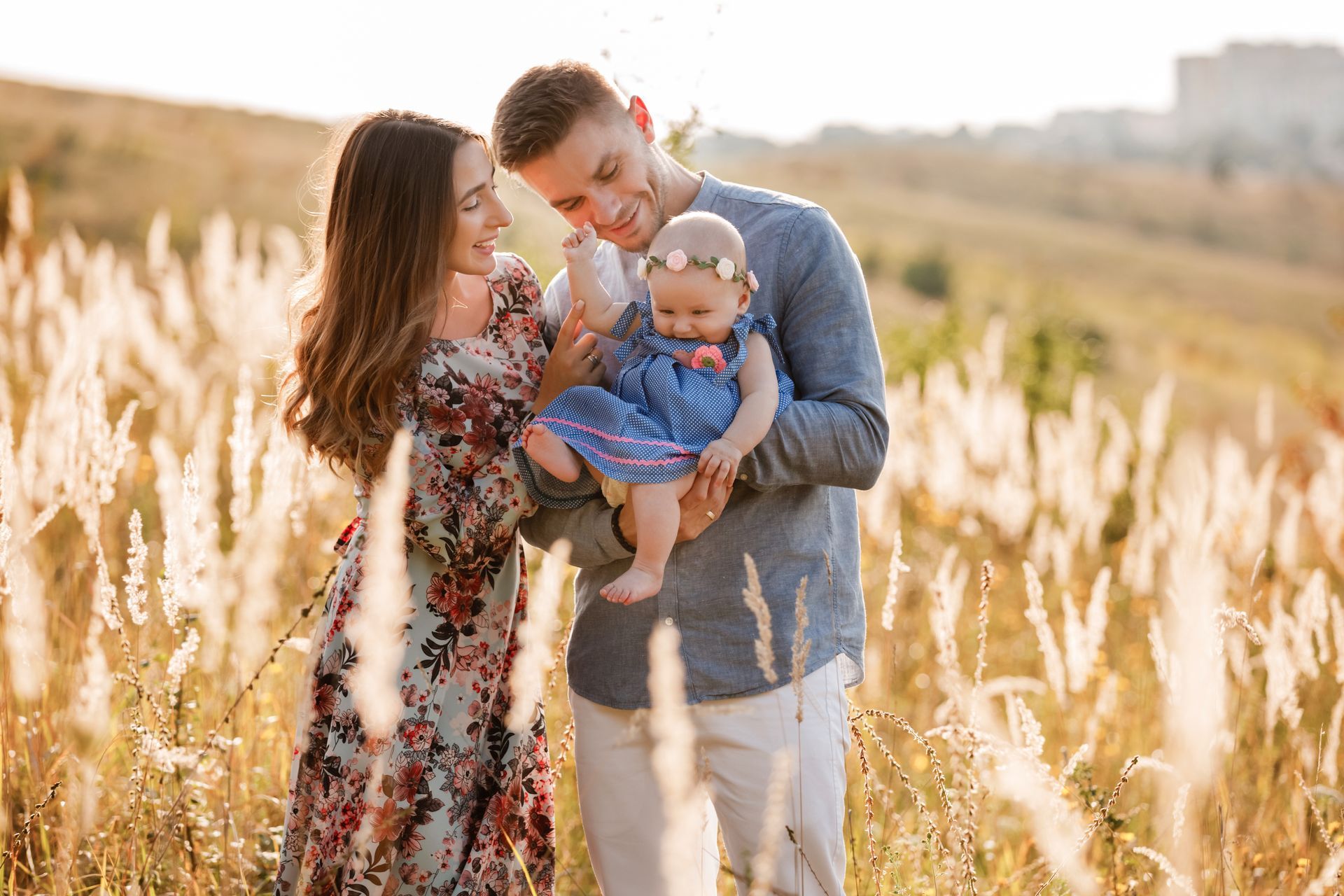 Papa et maman embrassent leur fille dans l'herbe au coucher du soleil