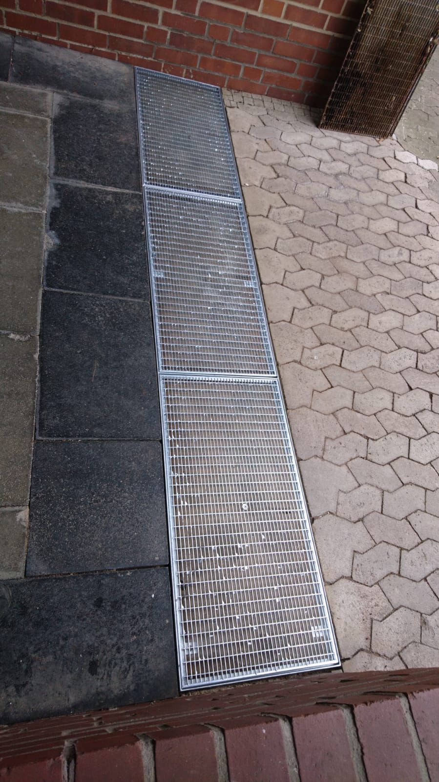 Auf einem gemauerten Gehweg neben einer Ziegelmauer steht eine Metallrampe.