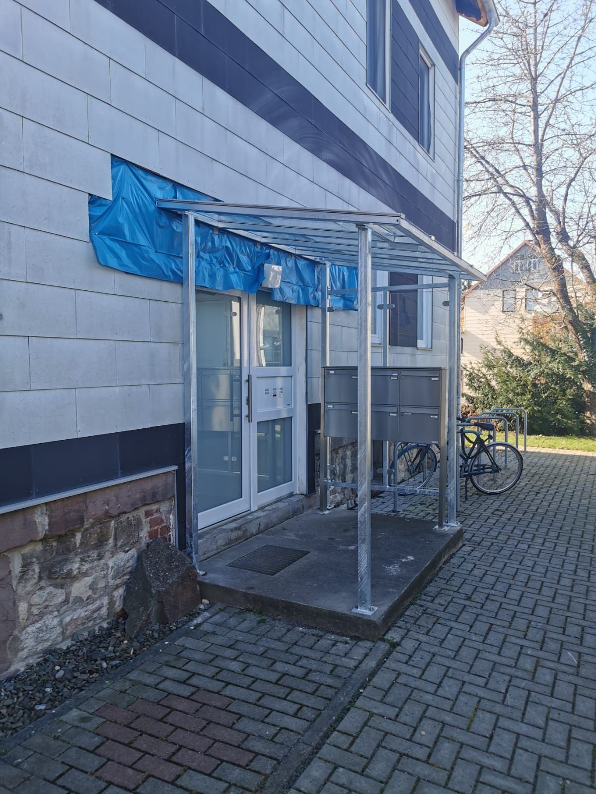 Ein gemauerter Gehweg führt zu einem Gebäude mit einem Vordach über dem Eingang.