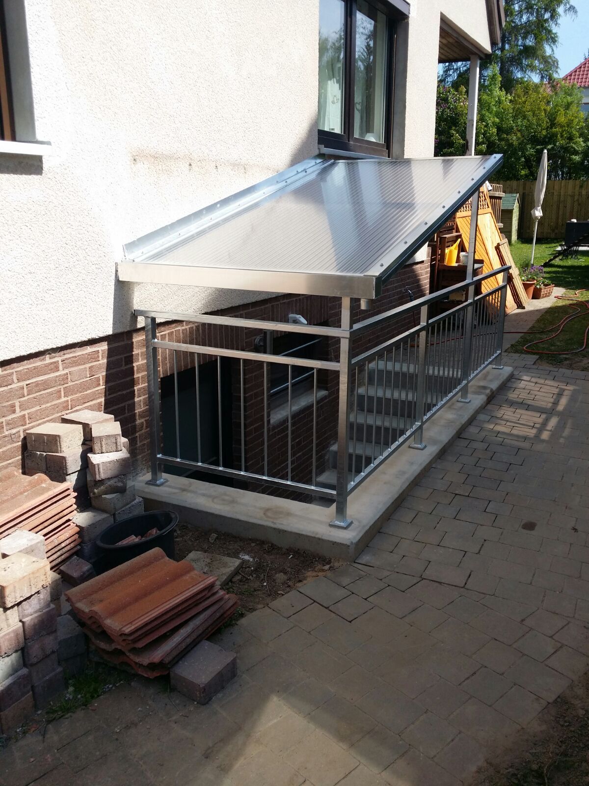 An der Seite eines Hauses ist ein Vordach und ein Geländer aus Edelstahl angebracht.