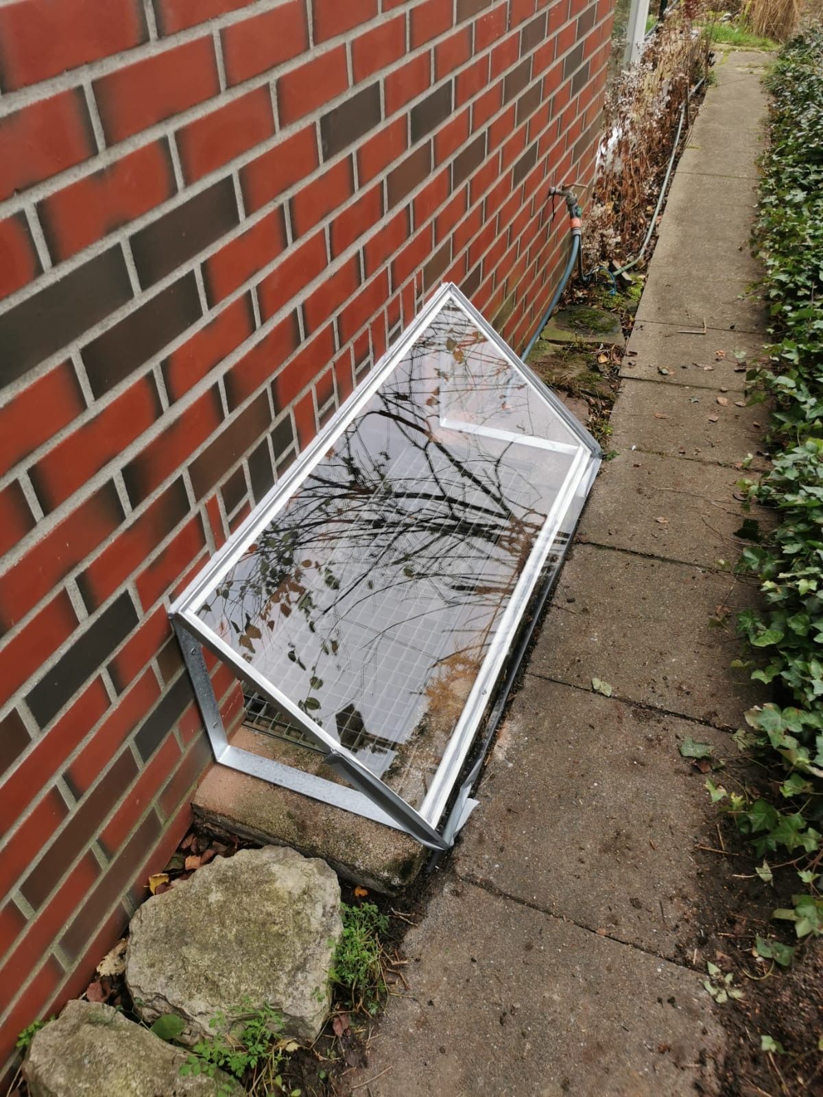 Auf dem Bürgersteig neben einer Backsteinmauer liegt eine Fensterabdeckung.