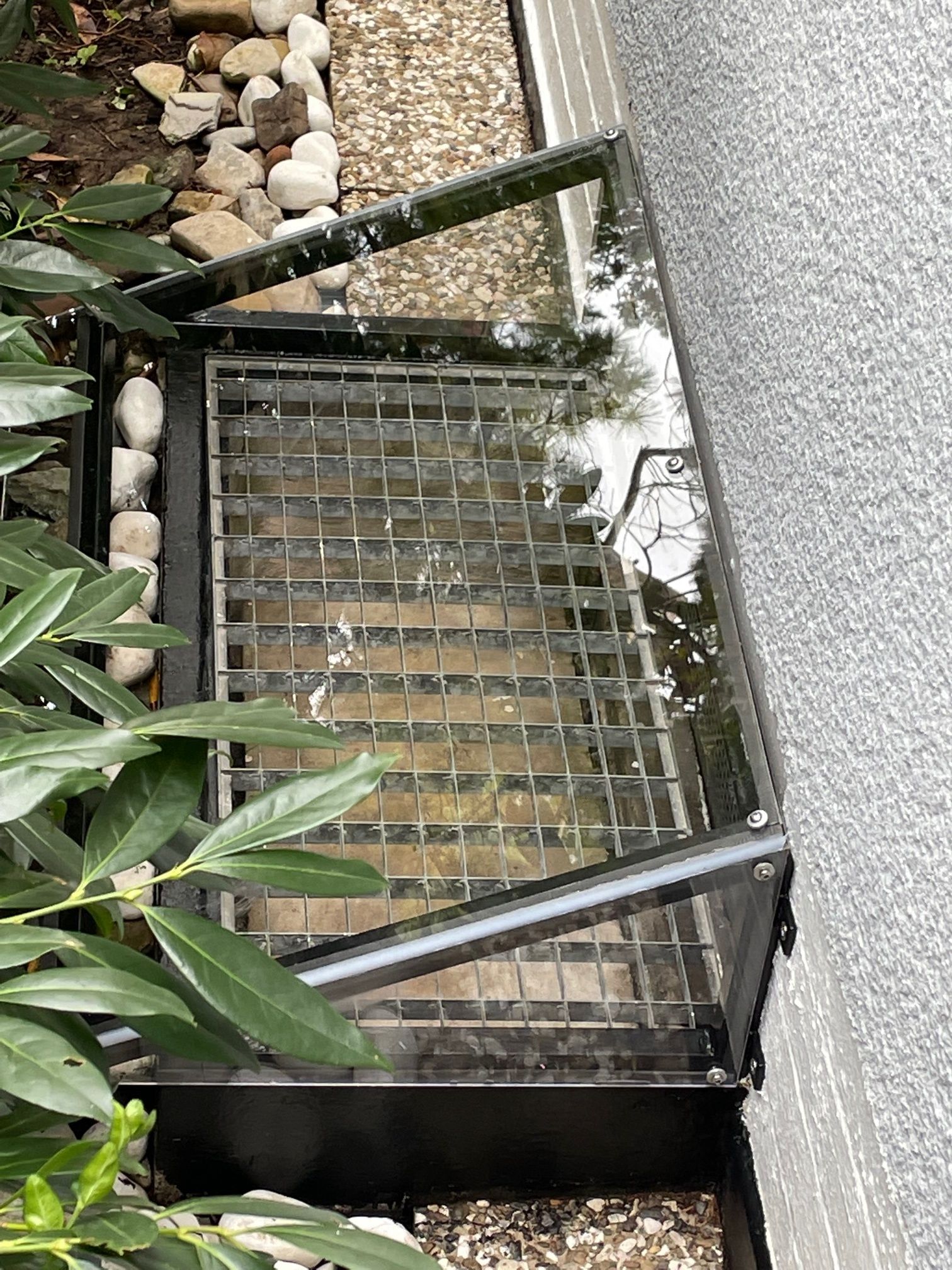 An der Seite eines Gebäudes neben einem Baum liegt ein Metallgitter.