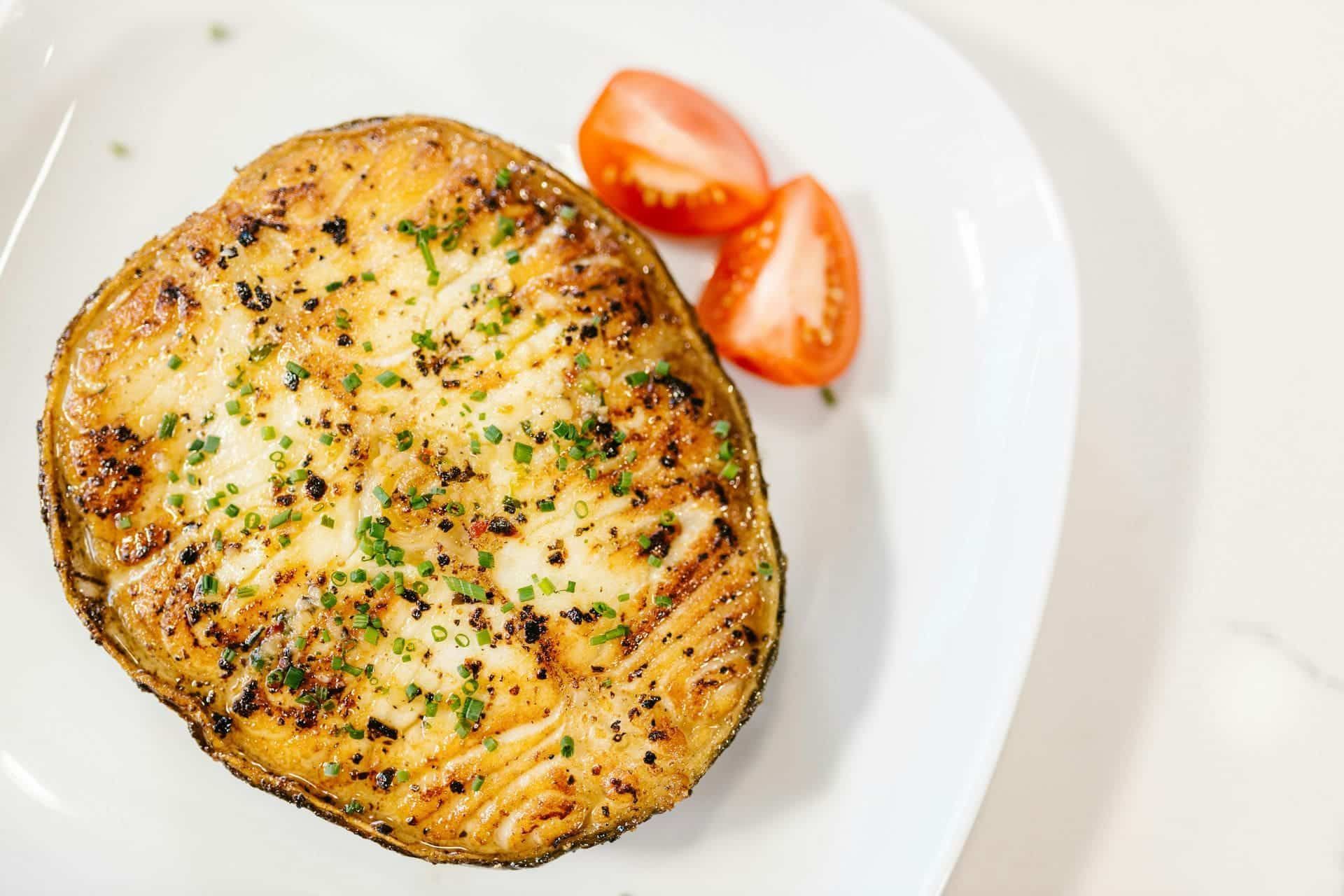 Filete de pescado a la parrilla en un plato blanco con dos gajos de tomate.