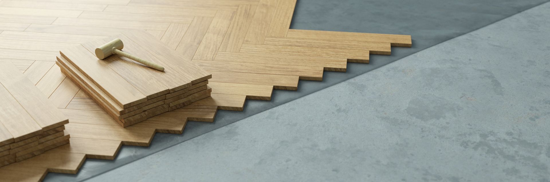 Des lames de parquet à chevrons sont installées sur un sous-plancher gris, avec une pile de bois et un petit outil en métal.