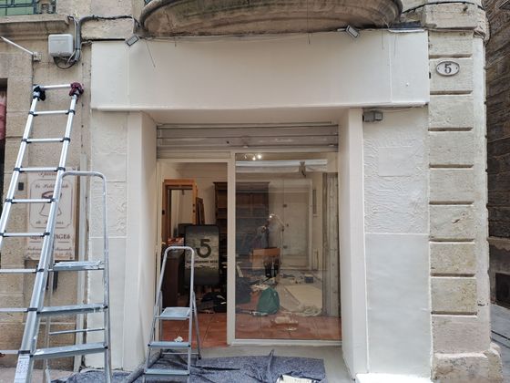 Une devanture de magasin en rénovation, avec une façade beige, des échelles et une entrée ouverte révélant un intérieur encombré.