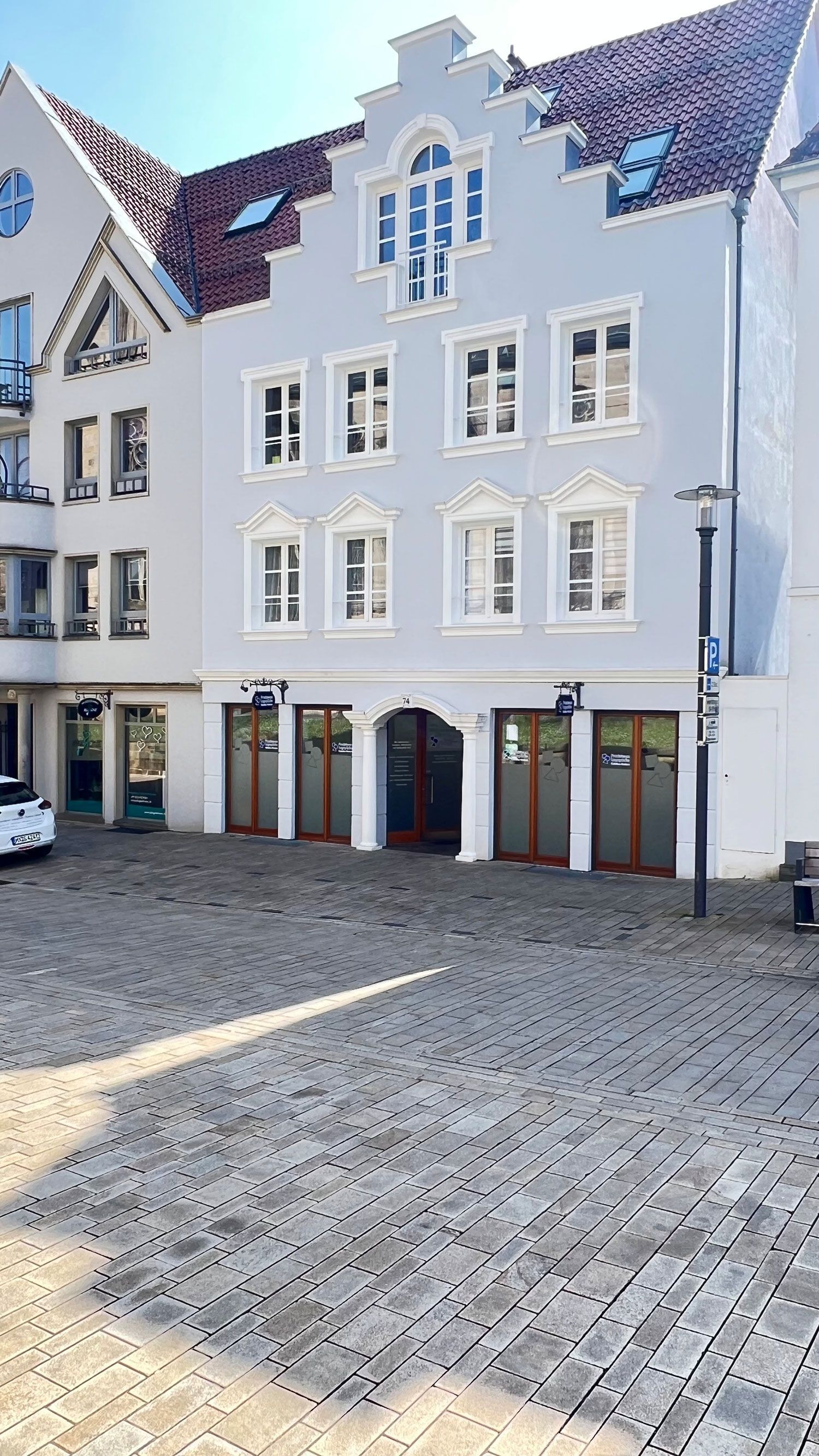 Ein hellblaues Gebäude mit Giebelfassade, Fenstern und Bogenläden an einer Kopfsteinpflasterstraße.