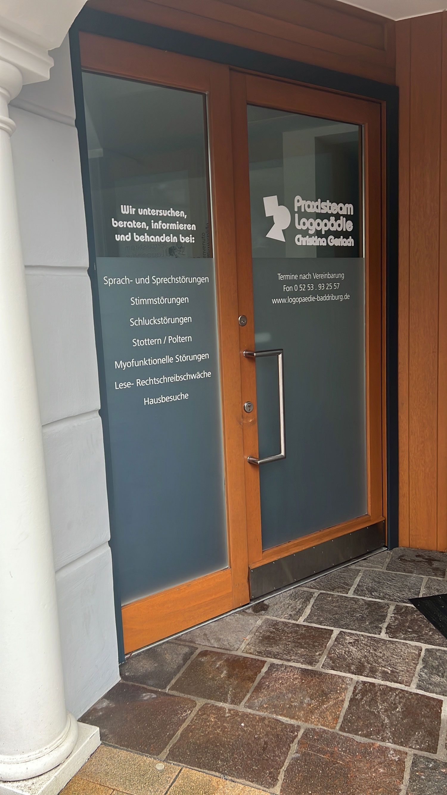 Doppelflügelige Holztüren einer Klinik mit Milchglasscheiben. Weißer Text und ein Logo sind sichtbar.