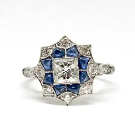 Un anillo de diamantes y zafiros con un diamante cuadrado en el centro.