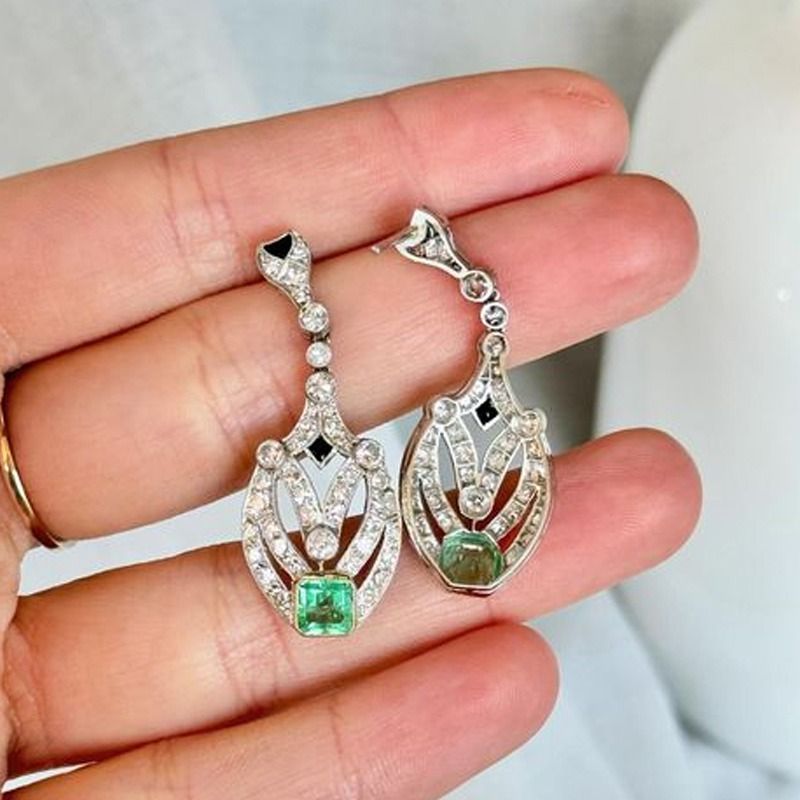 Una persona sostiene un par de pendientes con esmeraldas y diamantes.