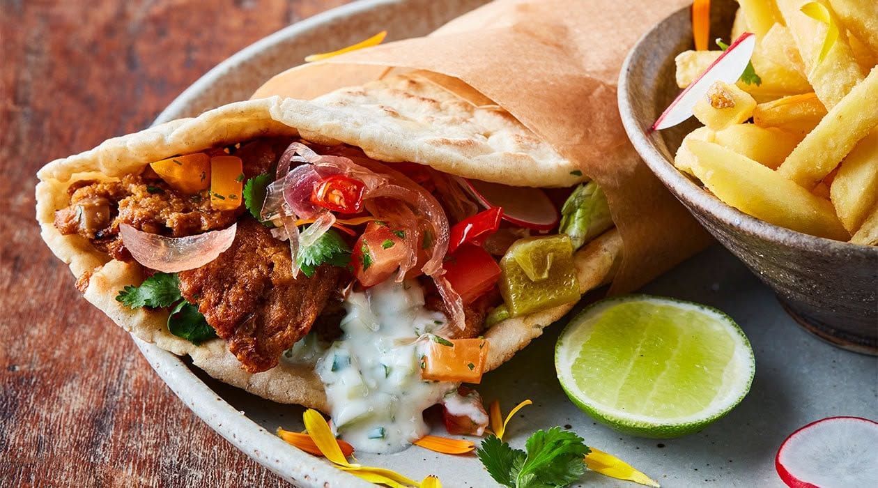Sándwich de pita con carne, verduras y salsa, acompañado de patatas fritas y una rodaja de lima