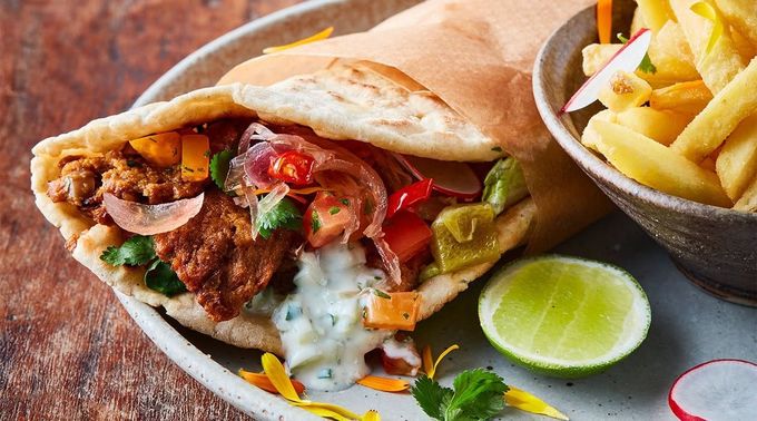Sándwich de pita con carne, verduras y salsa, acompañado de patatas fritas y una rodaja de lima