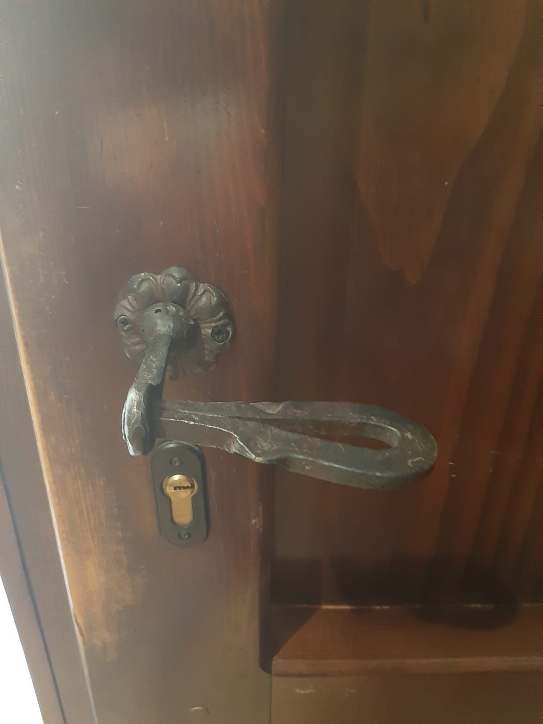 Un tirador y una placa de cerradura de metal oscuro y ornamentado, montados sobre una puerta de madera pulida.