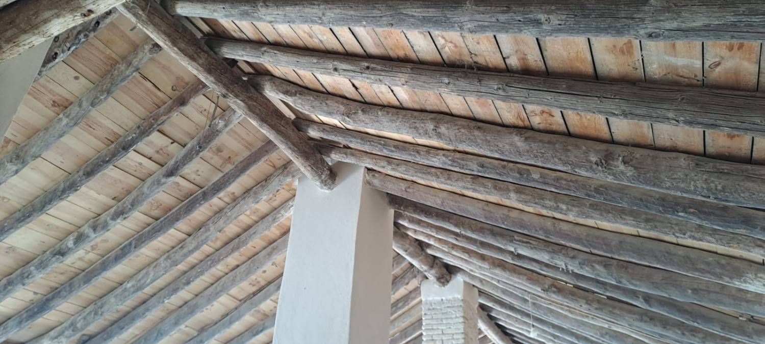 Vista desde un ángulo bajo de una estructura de techo de madera a la vista, con vigas y listones de madera que descansan sobre pilares de soporte interiores blancos.