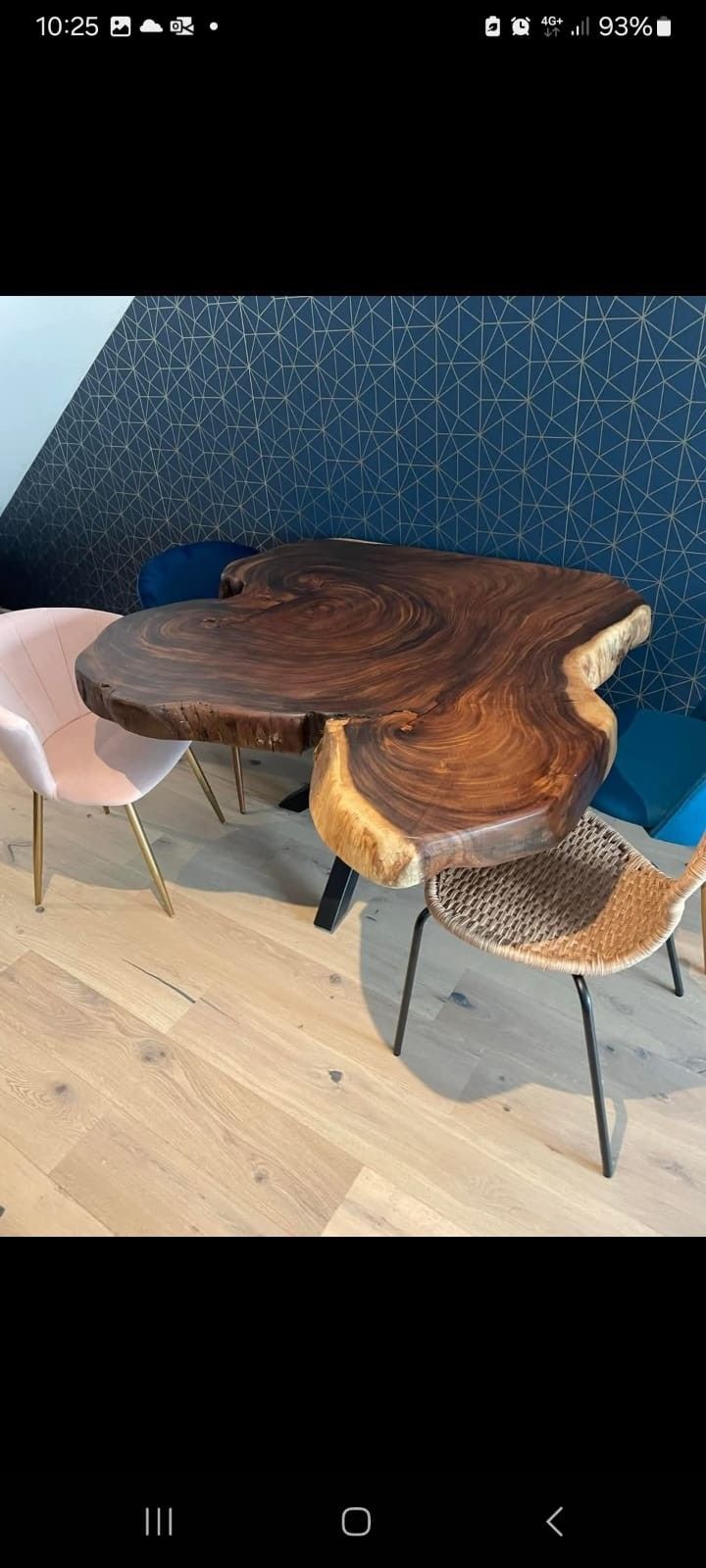 Una mesa de comedor de madera con borde natural y una gruesa tapa redondeada, combinada con modernas sillas rosas y tejidas en una habitación.