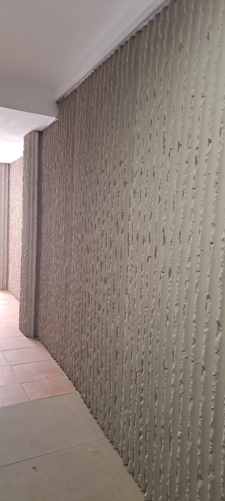 Un muro de hormigón texturizado de color claro con ranuras verticales se alza junto a un sendero pavimentado bajo un voladizo.