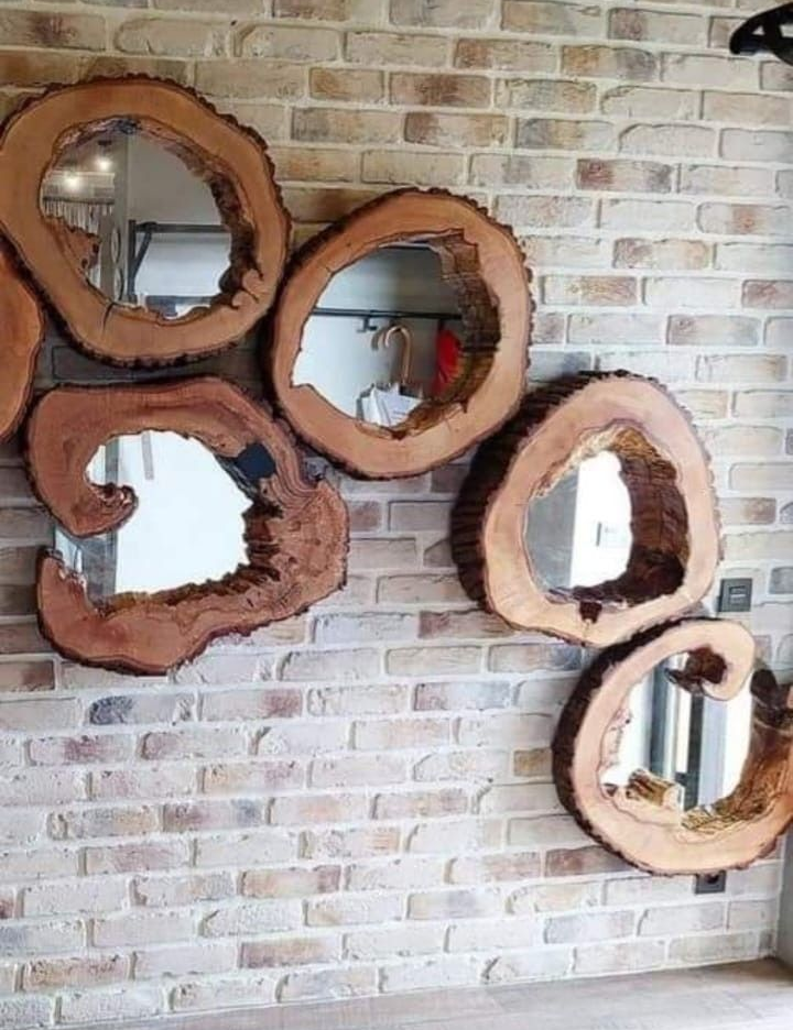 Cuatro espejos rústicos hechos con rodajas de madera natural están dispuestos sobre una pared de ladrillo de color claro.