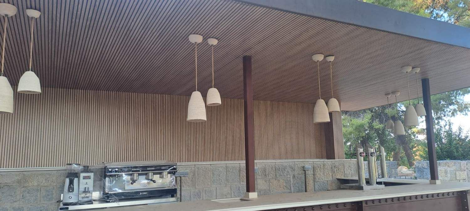 Un moderno bar al aire libre con mostradores de piedra, lámparas colgantes y revestimiento de pared decorativo con listones verticales de madera.
