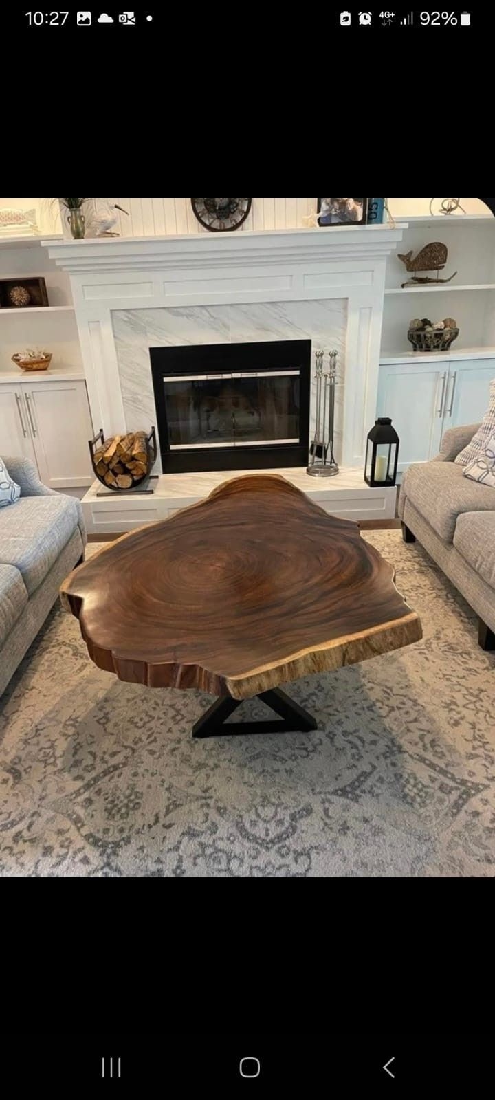 Una mesa de centro de madera con borde natural y base de metal descansa sobre una alfombra estampada en una sala de estar con chimenea.