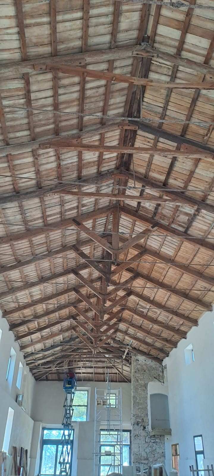 Un techo alto abovedado de madera con vigas a la vista cubre una habitación luminosa y diáfana con ventanas y una chimenea de piedra.