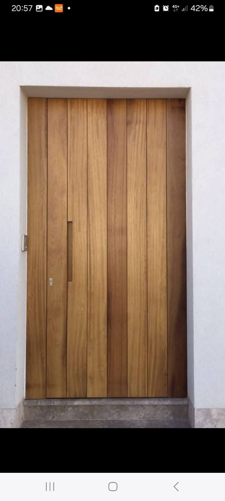 Una puerta moderna de madera con tablones verticales y un tirador largo y delgado, integrada en una pared blanca lisa.