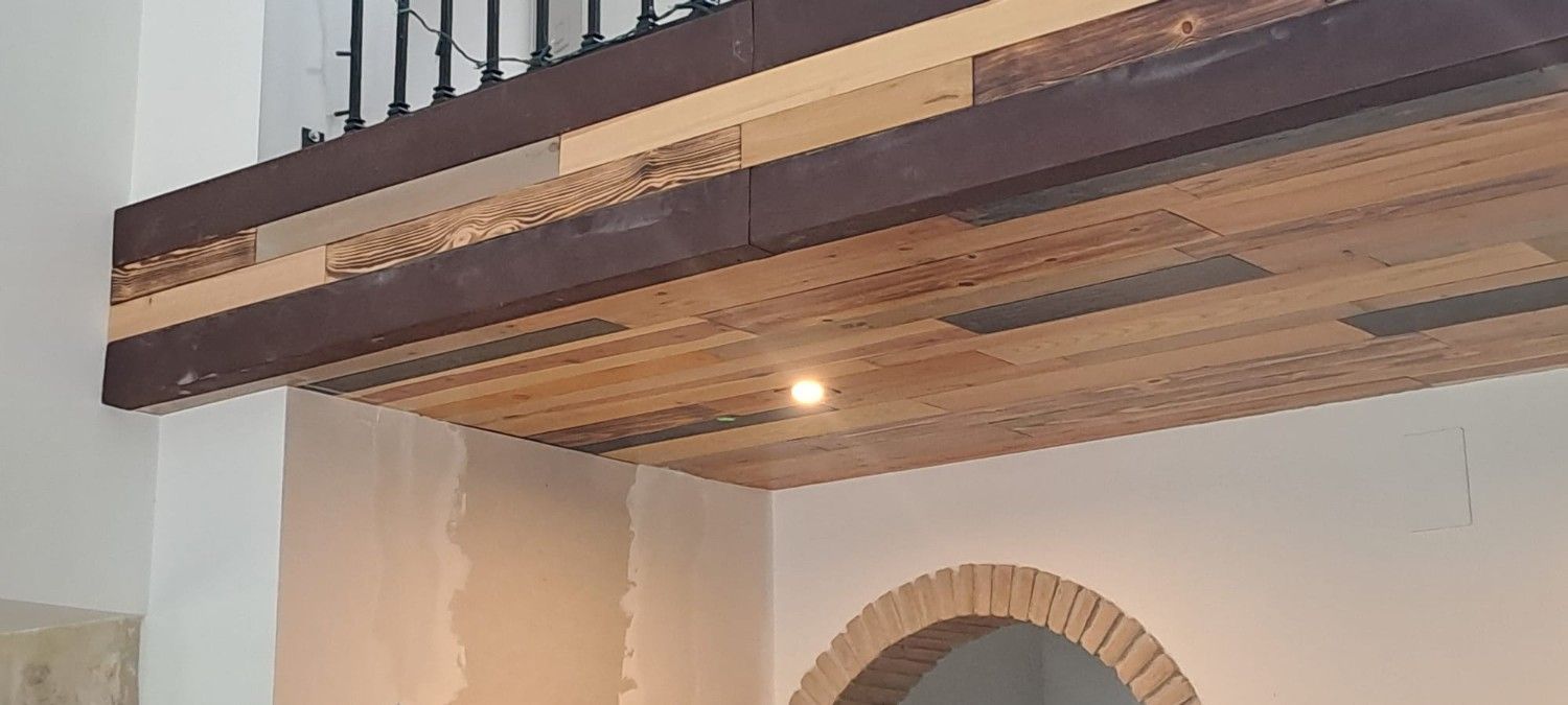 Vista desde un ángulo bajo de un techo de listones de madera con una luz incorporada, junto a una pared blanca y un arco de ladrillo.