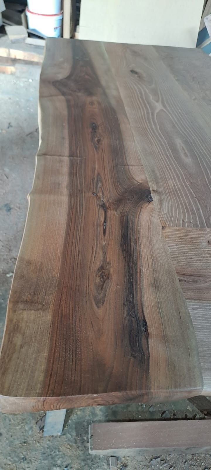 Primer plano de una mesa rústica de madera con borde natural y un prominente veteado oscuro y nudoso, en un entorno de taller.