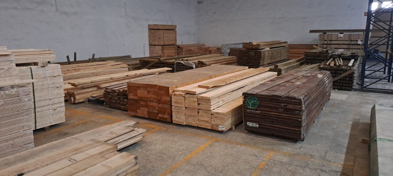 Interior de un almacén con pilas de vigas y tablones de madera de diversos tipos, organizados sobre el suelo de hormigón.
