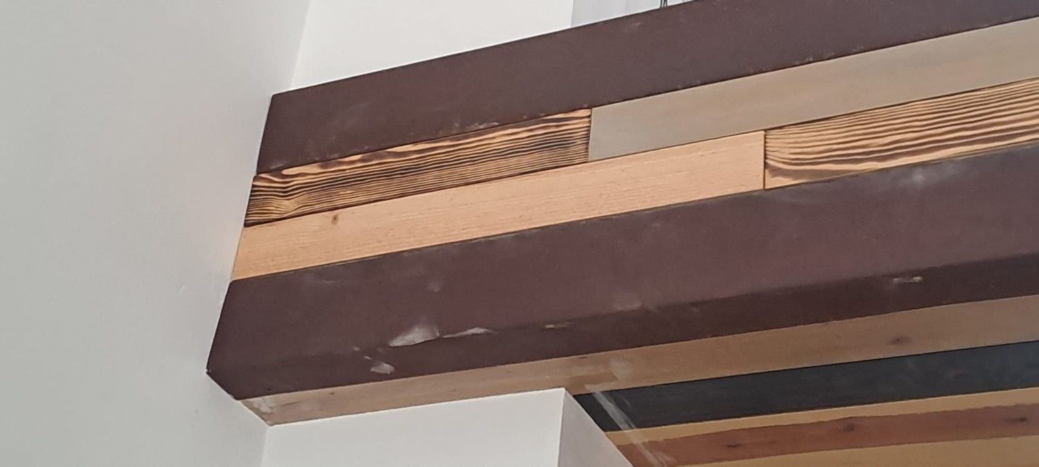 Una viga estructural contra una pared blanca que muestra materiales compuestos en capas, incluyendo madera, paneles oscuros y capas texturizadas.
