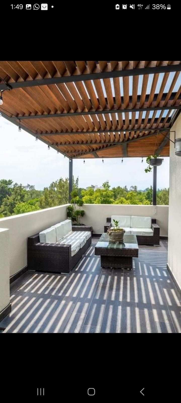 Una terraza en la azotea con una pérgola de madera con listones, asientos de mimbre oscuro con cojines blancos y una mesa de centro.