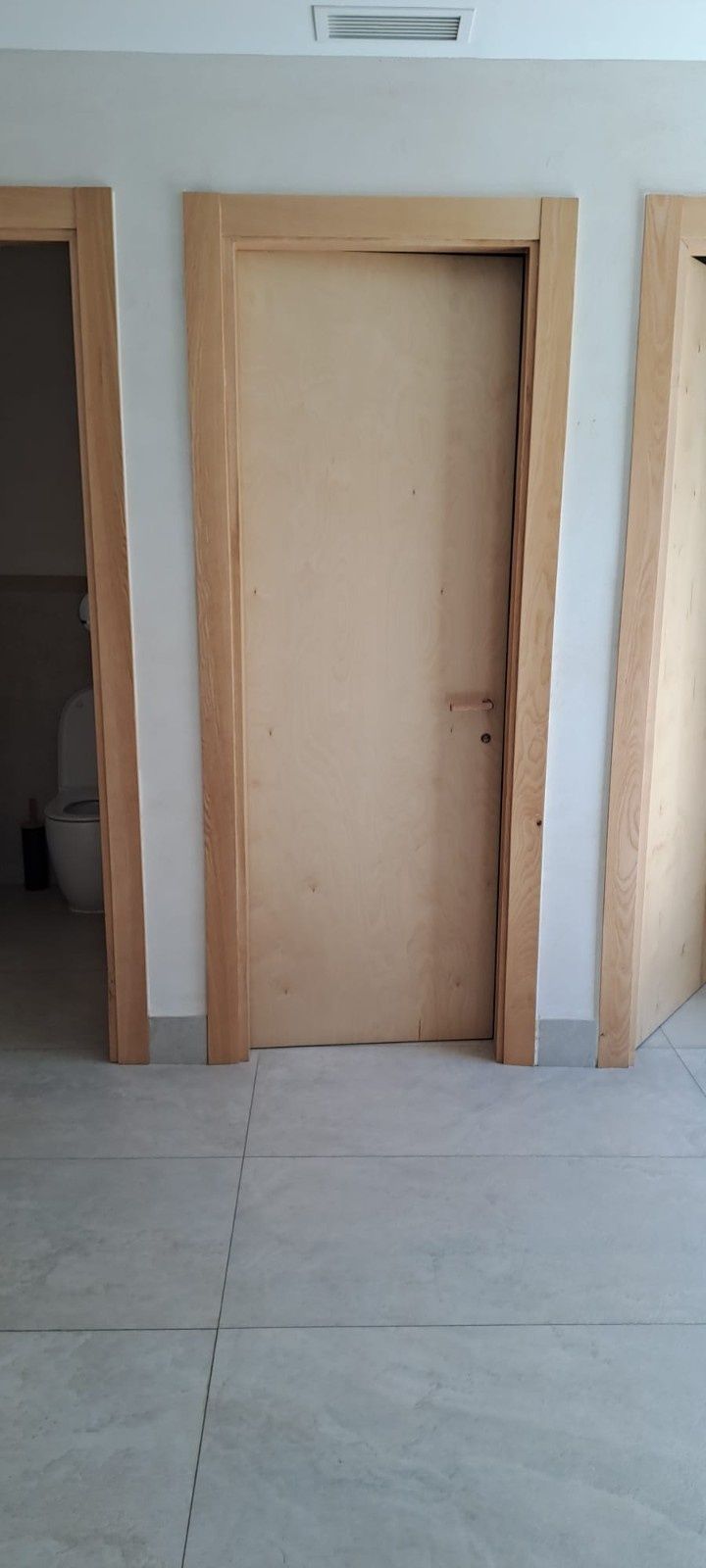 Tres puertas de madera en un pasillo interior de color claro con suelo de baldosas.