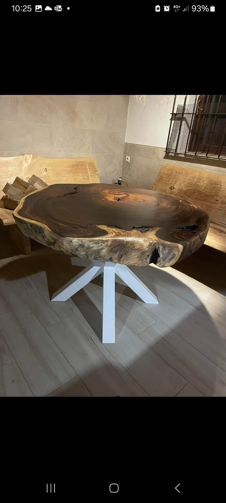 Una mesa de comedor circular de madera oscura con borde natural y una base metálica blanca de cuatro patas en una habitación.