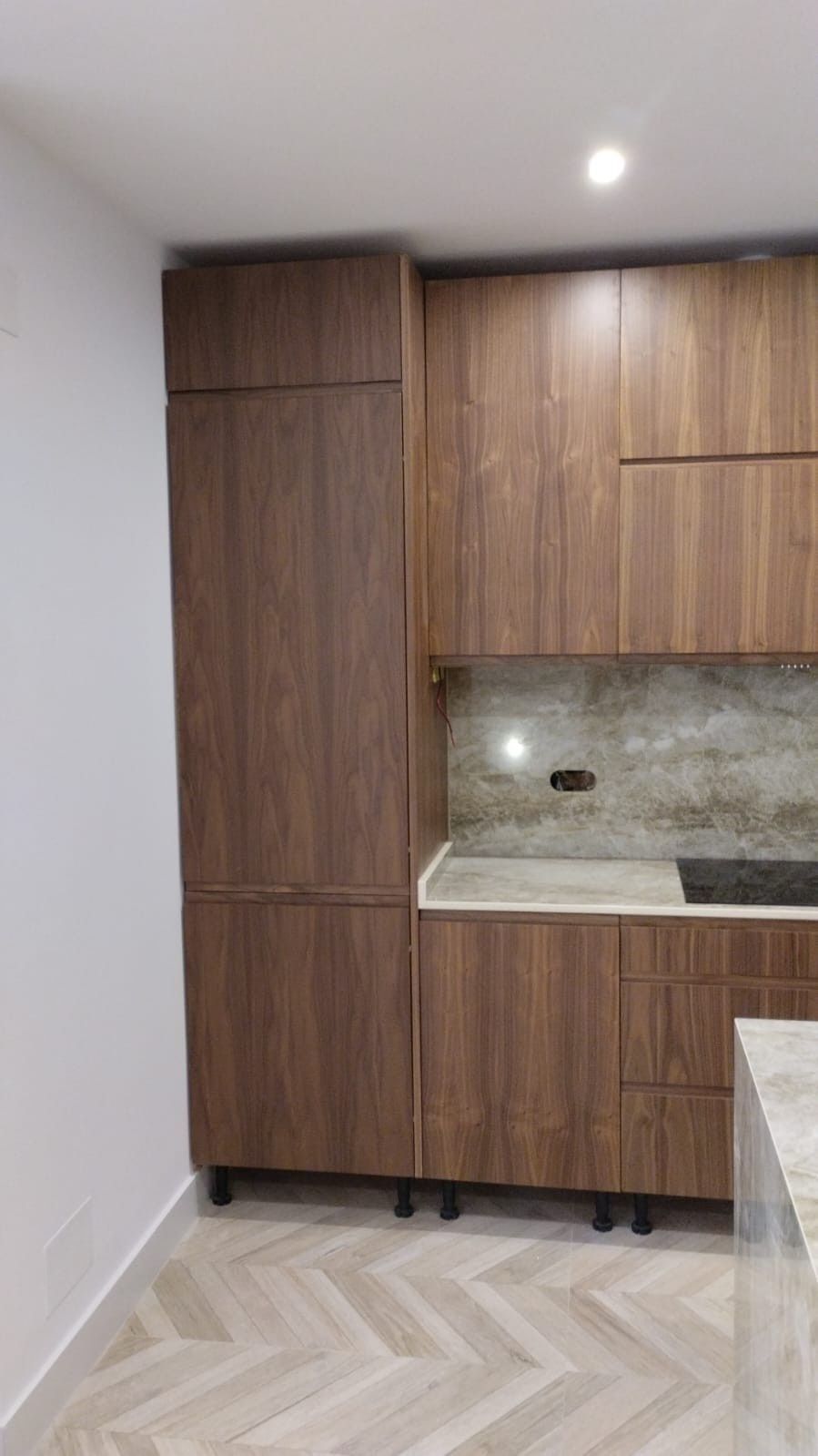 Una cocina moderna cuenta con gabinetes de madera oscura, una encimera de piedra clara y un piso de espiga de color claro.