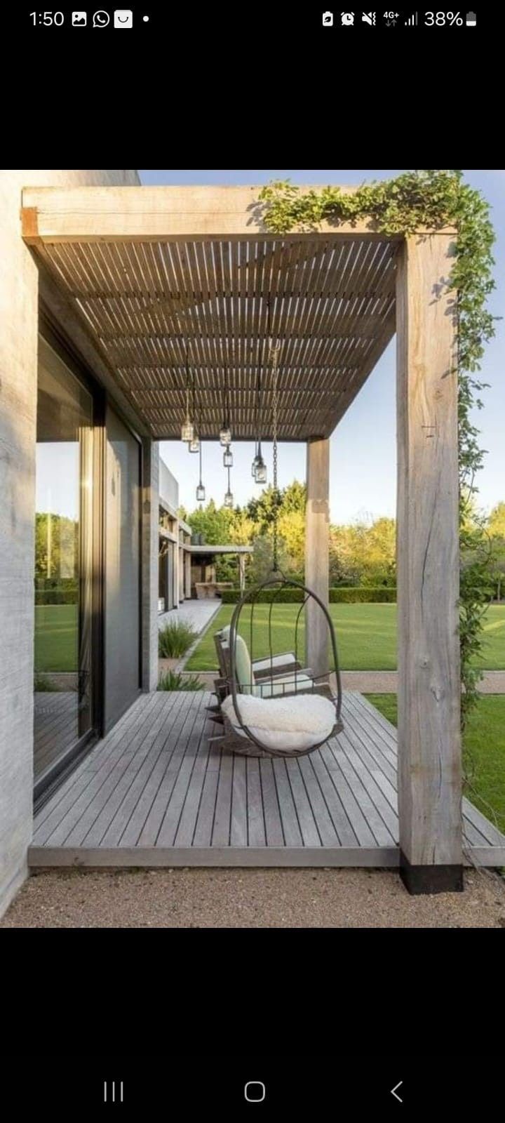Una pérgola de madera sobre una terraza con sillas colgantes, con vistas a un césped al atardecer.