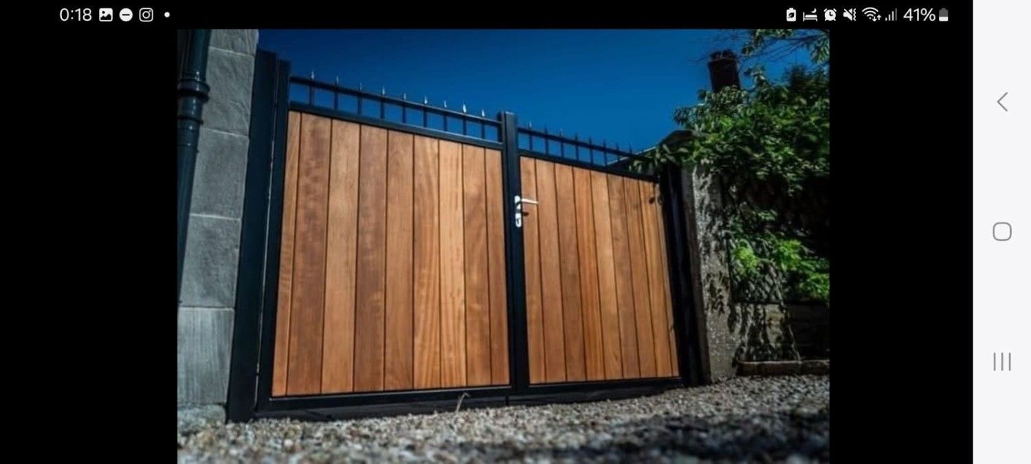 Una puerta moderna con tablones de madera verticales enmarcados en metal negro con pinchos decorativos, colocada contra un muro de piedra.